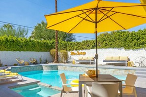 A pool area with lounge chairs, a table with chairs, and a yellow umbrella.