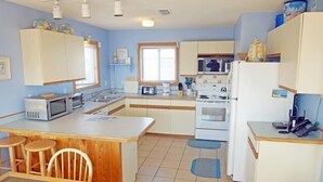 A compact kitchen with a central island, a refrigerator, a microwave, and a stove. There are wooden chairs and a small table at the island. - OS602- Private Pool, Hot Tub, WIFI, Oceanviews, Just Steps to the Beach! (Corolla)