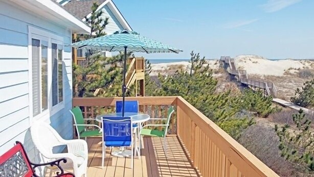 A wooden deck with a table and chairs, overlooking a beach with sand dunes and a wooden walkway. - OS602- Private Pool, Hot Tub, WIFI, Oceanviews, Just Steps to the Beach! (Corolla)