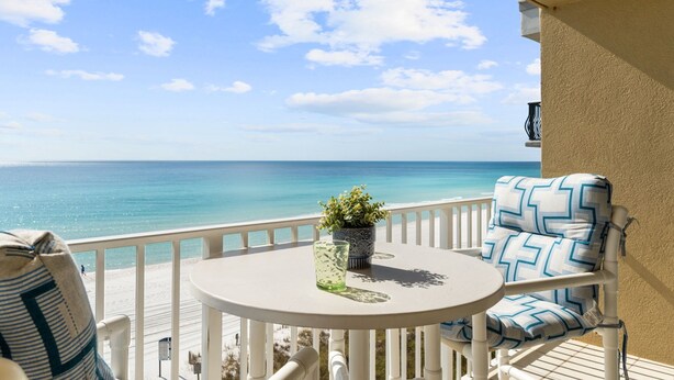 A balcony with a view of the ocean, a round table, a chair with patterned cushions, and a potted plant.