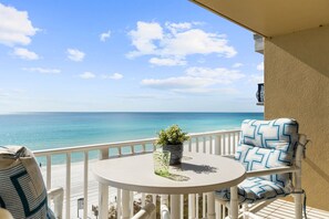 A balcony with a view of the ocean, a round table, a chair with patterned cushions, and a potted plant. - SL 505: Coral Sands - Golden Hour Every Hour Here on the Gulf!! (Fort Walton Beach)