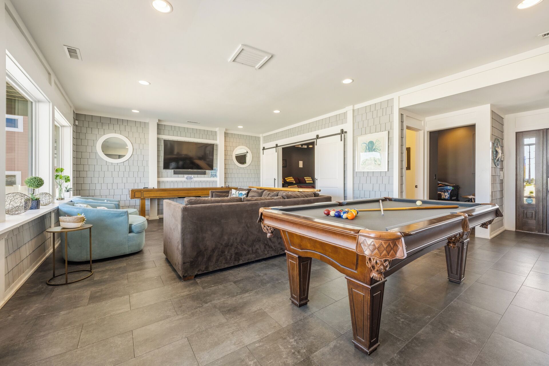 Un salon moderne avec une table de billard, des canapés gris et un téléviseur.