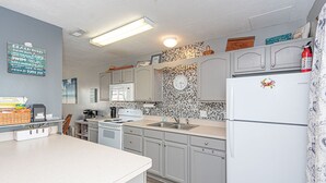 A kitchen with white cabinets, a microwave, a sink, and a refrigerator. There is a clock on the wall and a fire extinguisher near the refrigerator. - Fun, colorful 3-bedroom townhouse with free WiFi and a partial ocean view located midtown on the ocean block and just a short walk to the beach! (OCEAN CITY)