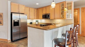 Una cocina moderna con armarios de madera, electrodomésticos de acero inoxidable y una isla central con taburetes de bar.