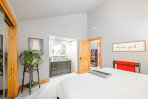 A bedroom with a bed, a dresser, a mirror, a plant, a red towel, and a sign on the wall.