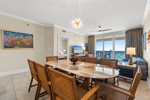 A dining area with a round table, chairs, a ceiling fan, and a view of the ocean. - Azure 504: Tranquil Tides - Where the Waves Meet the Shore! (Fort Walton Beach)