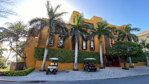 Un edificio con facciata gialla, palme e due golf cart parcheggiate davanti.
