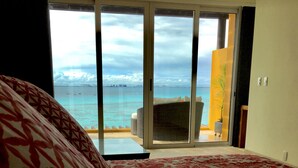 Camera da letto con un letto grande, vista sul mare tramite una porta scorrevole in vetro e un balcone con una sedia e una pianta.