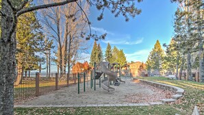 Ein Spielplatz mit Rutsche und Klettergerüst, umgeben von Bäumen und einem eingezäunten Bereich.