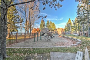 Un parque infantil con tobogán y estructura de escalada, rodeado de árboles y una zona vallada.