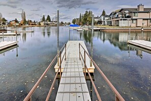 Une jetée en bois mène à une étendue d’eau calme, avec des maisons en arrière-plan.