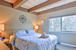 Une chambre à coucher avec un lit, une fenêtre donnant sur des arbres, un élément de décoration murale et une lampe de chevet.