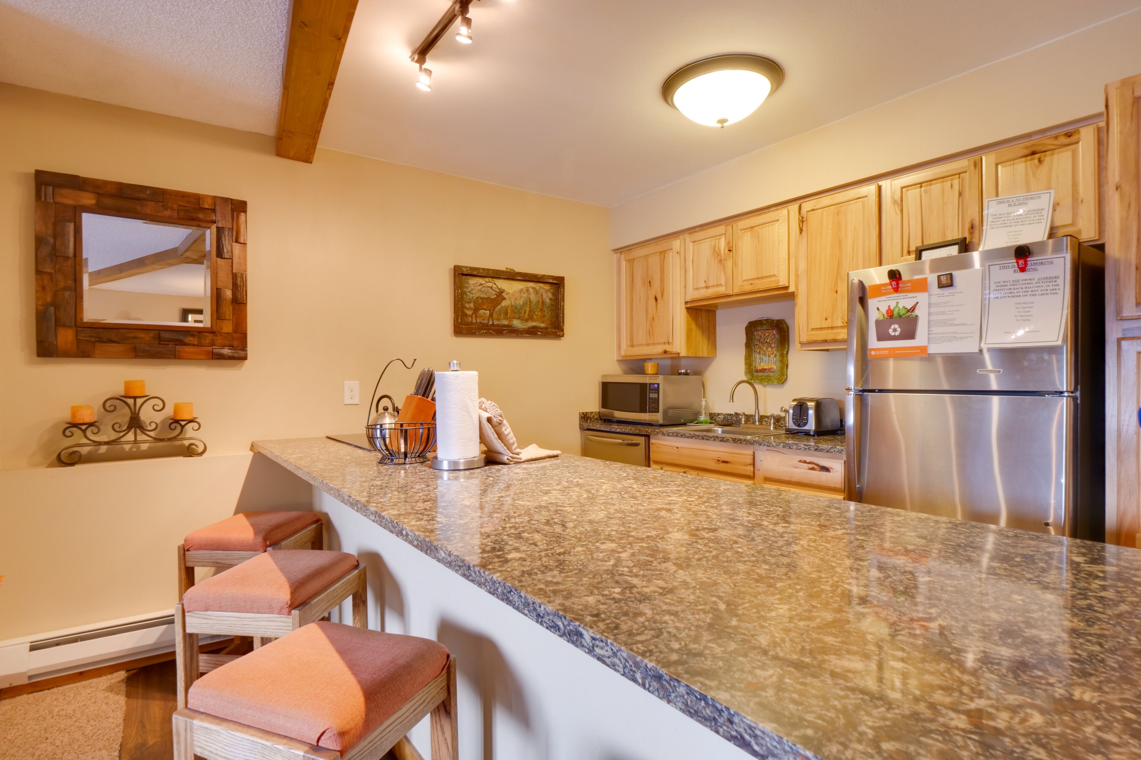 A kitchen with granite countertops, wooden cabinets, a stainless steel refrigerator, and a microwave.