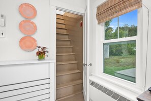 A bathroom with a white door, a window with a view of the outdoors, and a wall-mounted plate rack. - Charming Cape Cottage Steps from Bank St Beach (Harwich Port)