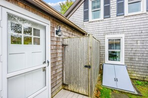 A residential property with a wooden garage door, a white door, and a window with shutters. - Charming Cape Cottage Steps from Bank St Beach (Harwich Port)