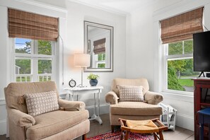 A living room with two armchairs, a small table with a lamp, a television, and a large mirror on the wall.