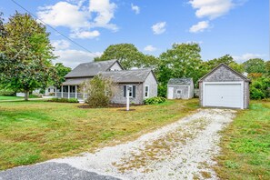 A residential area with a gravel driveway leading to a house with a porch and a garage. - Charming Cape Cottage Steps from Bank St Beach (Harwich Port)