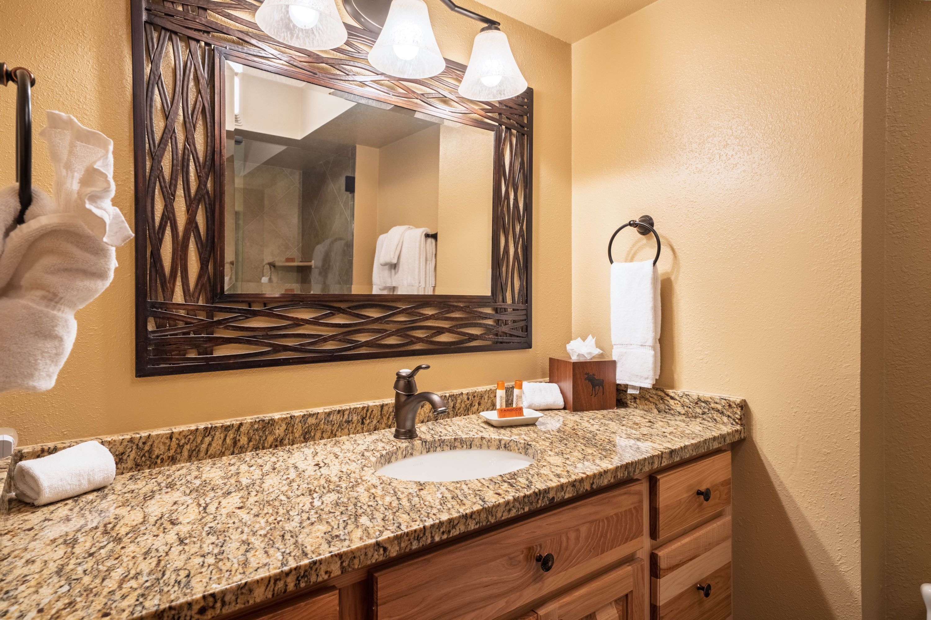 A bathroom with a granite countertop, a sink, a mirror with lights, and a towel rack.