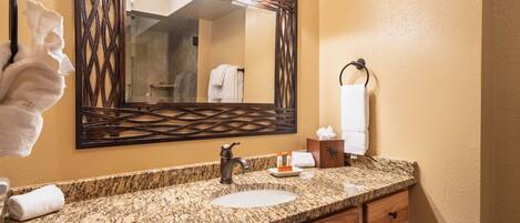 A bathroom with a granite countertop, a sink, a mirror with lights, and a towel rack.