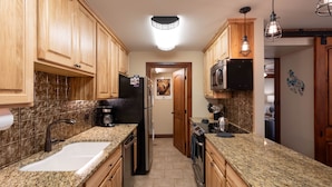 Una cocina con gabinetes de madera, encimeras de granito, electrodomésticos de acero inoxidable e iluminación colgante.