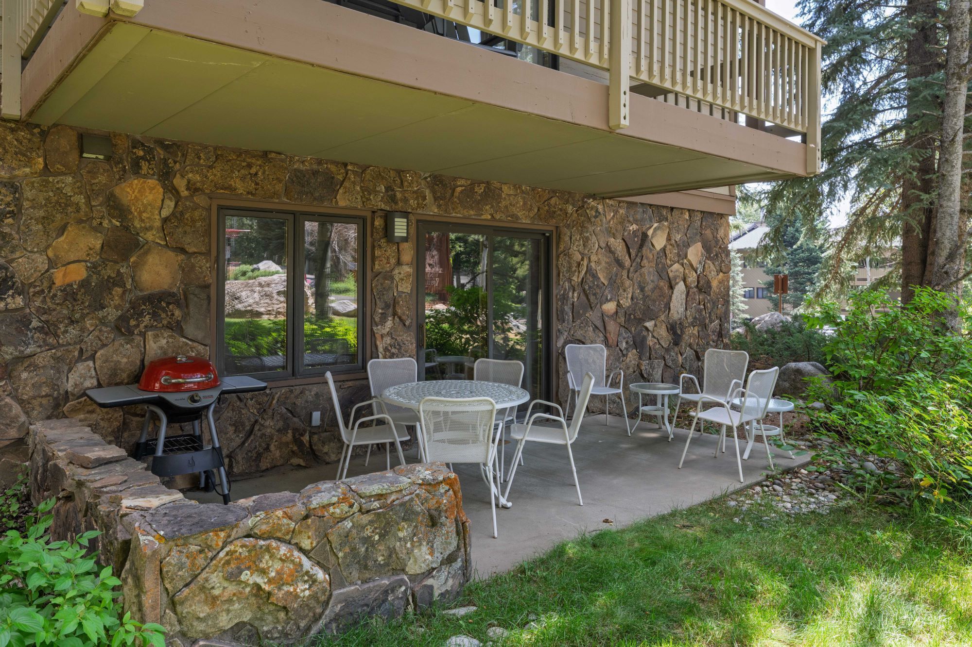 An outdoor patio with stone walls, a grill, and white wicker chairs.