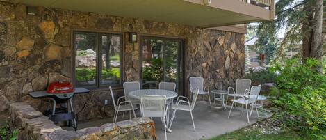 An outdoor patio with stone walls, a grill, and white wicker chairs.