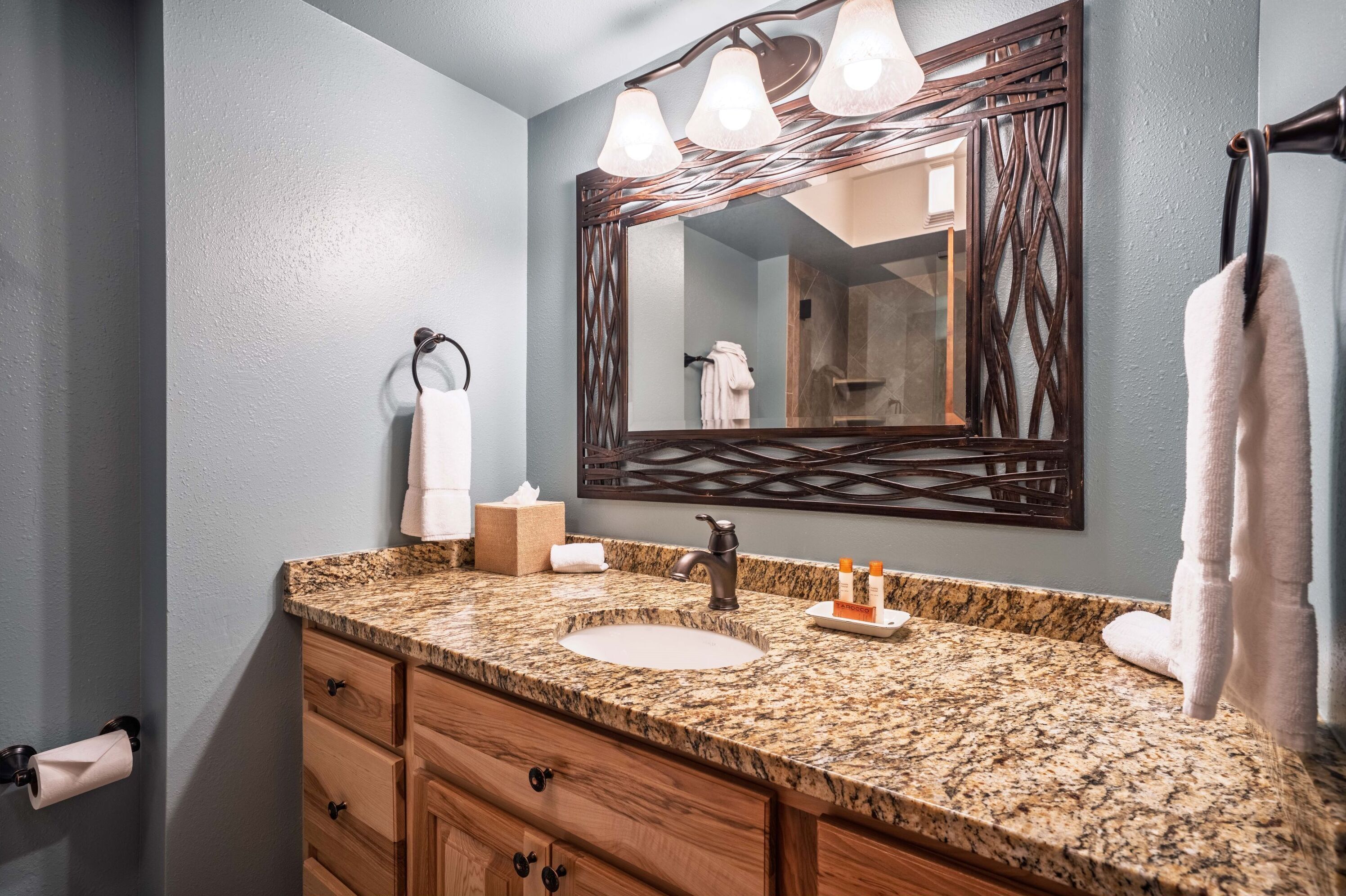 A bathroom with a granite countertop, a sink, a mirror with a decorative frame, and a towel rack.