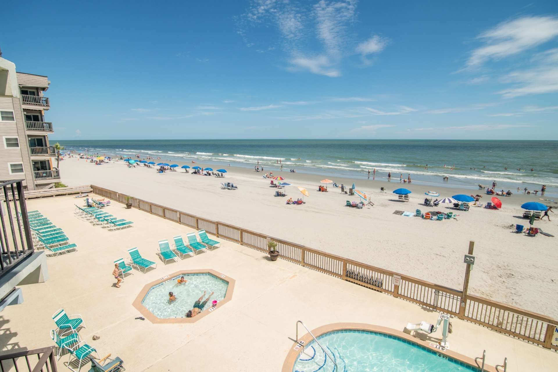 A beach view with a pool area, lounge chairs, and umbrellas.