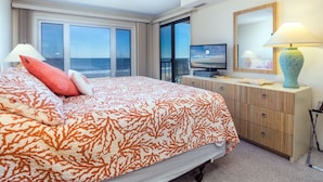 A hotel room with a large bed, a television, a desk with a lamp, and a view of the ocean. - Enjoy panoramic views of the beach from the living room, dining room, kitchen and master bedroom. (Ocean City)