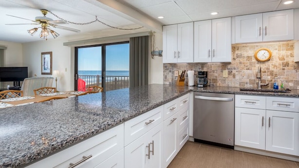 A kitchen with white cabinets, granite countertops, and a view to the outside. - Enjoy panoramic views of the beach from the living room, dining room, kitchen and master bedroom. (Ocean City)