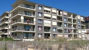 A multi-story residential building with balconies, a sandy ground floor, and a wooden fence. - Enjoy panoramic views of the beach from the living room, dining room, kitchen and master bedroom. (Ocean City)