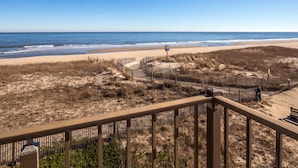 A beach view from a balcony with a wooden railing, sandy beach, and ocean. - Enjoy panoramic views of the beach from the living room, dining room, kitchen and master bedroom. (Ocean City)
