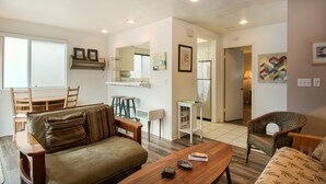 A living room with a sofa, a coffee table, and a wicker chair. There is a dining area with a table and chairs.