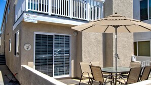 A two-story house with a balcony, a patio with a table and chairs, and a large umbrella.