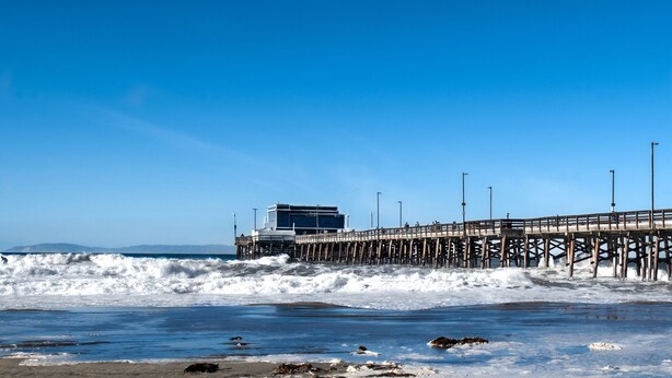 A pier with a building at the end, extending into the ocean with waves crashing against it.