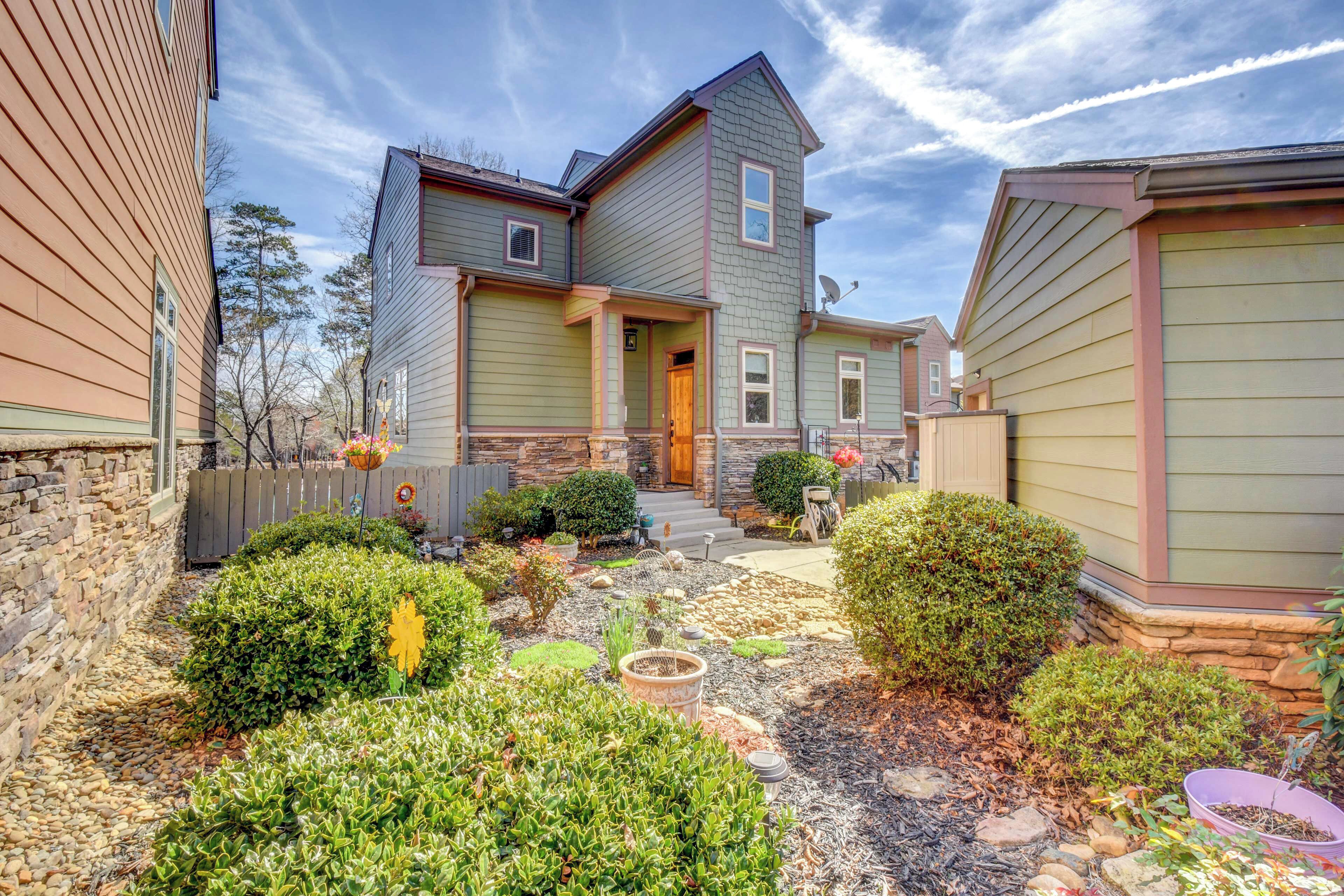 A two-story house with a stone foundation, a front porch, and a well-maintained garden with various plants and a fire pit.