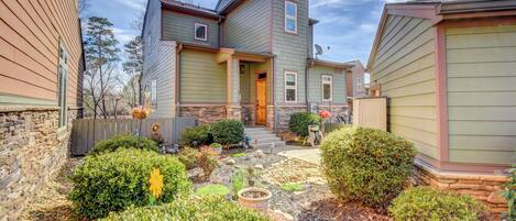 A two-story house with a stone foundation, a front porch, and a well-maintained garden with various plants and a fire pit.