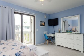 Une chambre à coucher comprenant un lit, un bureau, une chaise, une commode, une télévision et un balcon.