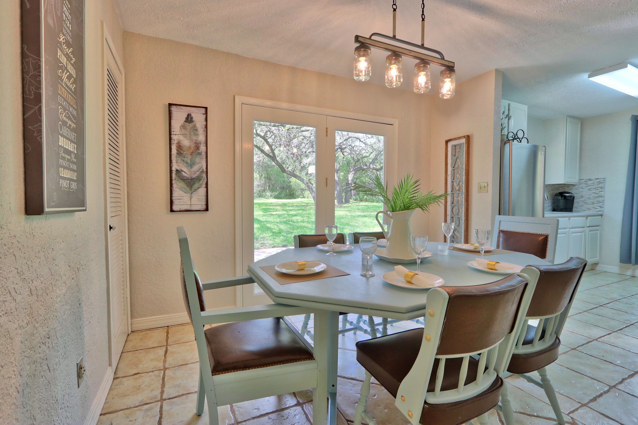 A dining area with a table set for four, a chandelier, and a view of the outdoors.