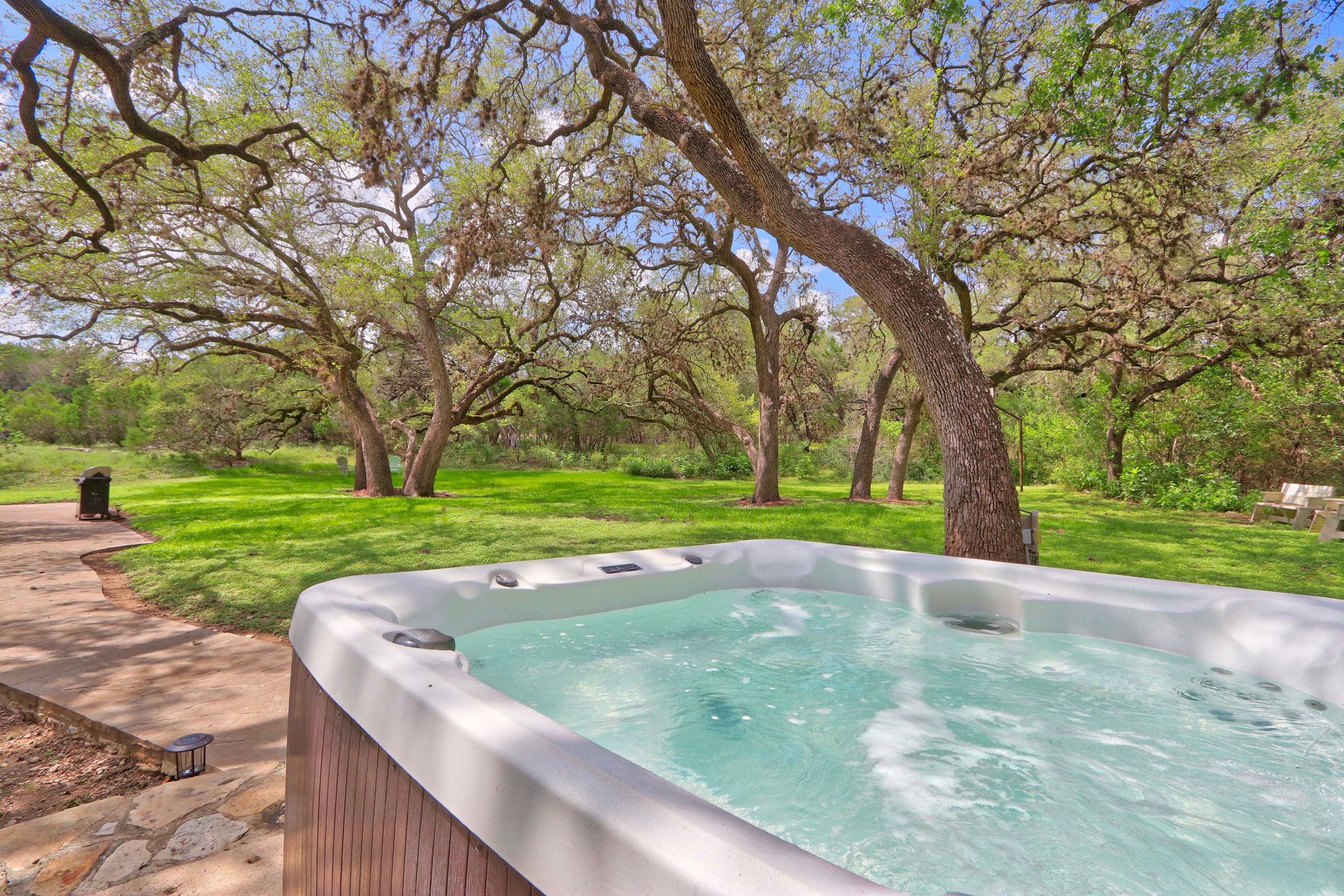 A hot tub in a lush garden with a stone pathway and a wooden deck.