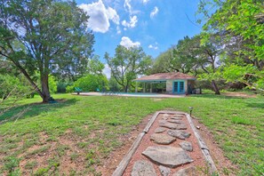 A covered outdoor area with a stone pathway leading to a building, surrounded by trees and a grassy lawn.