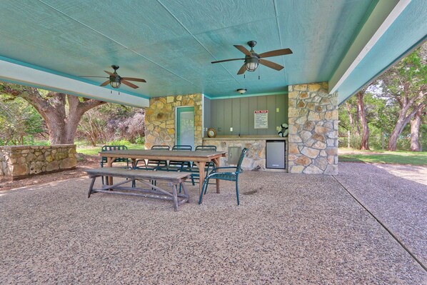 An outdoor covered picnic area with a table and chairs, a stone wall, and a ceiling fan.