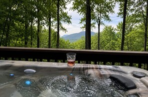 Jacuzzi amb una beguda i vistes a un bosc i muntanyes.
