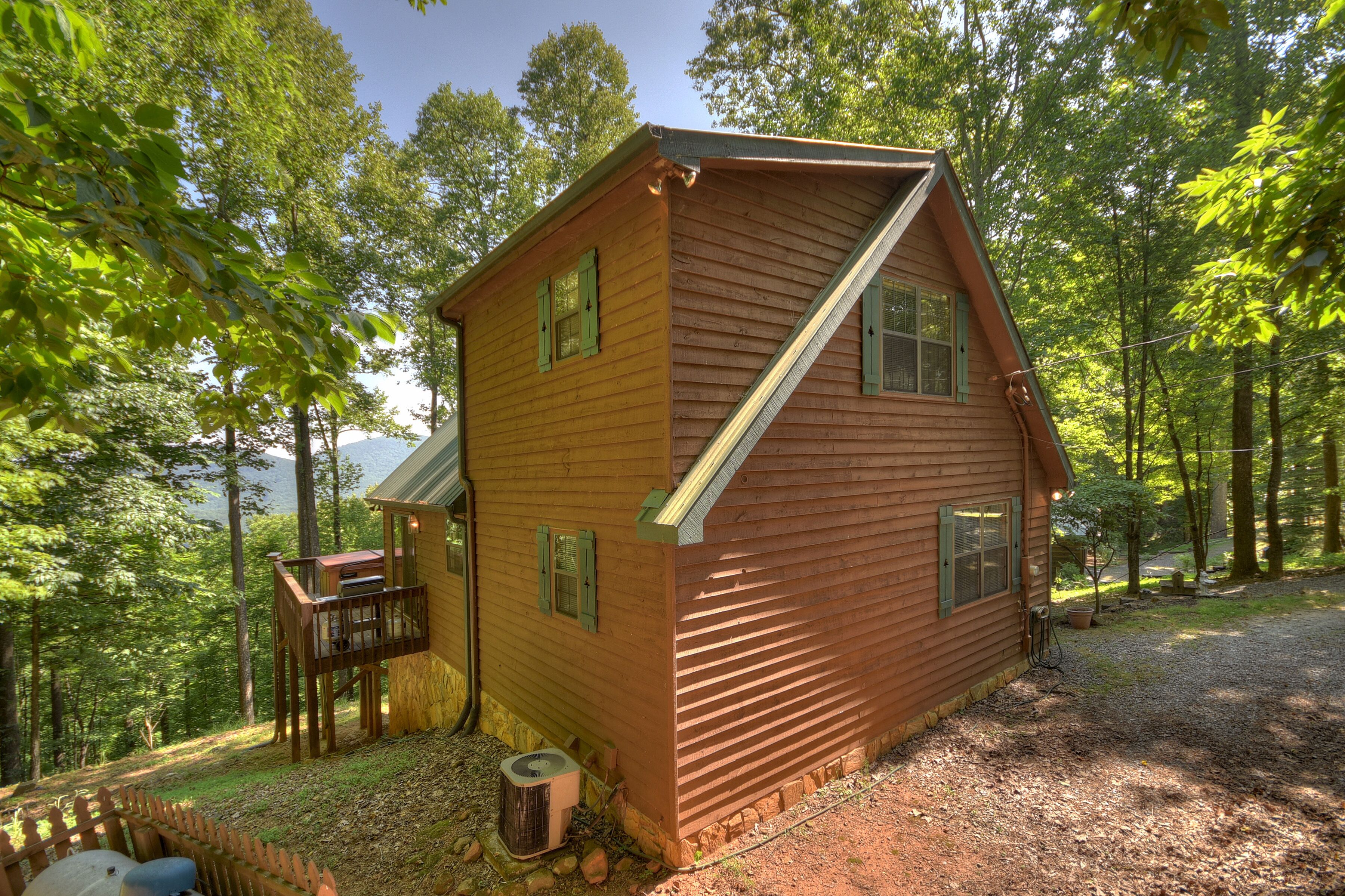 A wooden cabin with a deck, surrounded by trees.