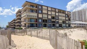 A multi-story hotel with balconies, located near a sandy beach. - Well maintained 1 BR, 1.5 BA oceanfront condo. Enjoy the beautiful ocean views from your balcony and inside the unit. (Ocean City)