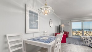 A dining area with a table and chairs, a chandelier, a framed picture on the wall, a clock, and a view of the beach through large windows. - Well maintained 1 BR, 1.5 BA oceanfront condo. Enjoy the beautiful ocean views from your balcony and inside the unit. (Ocean City)