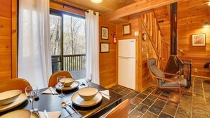 L’intérieur d’une cabane en bois, avec une table à manger dressée pour quatre personnes, une chaise, un poêle et un réfrigérateur.
