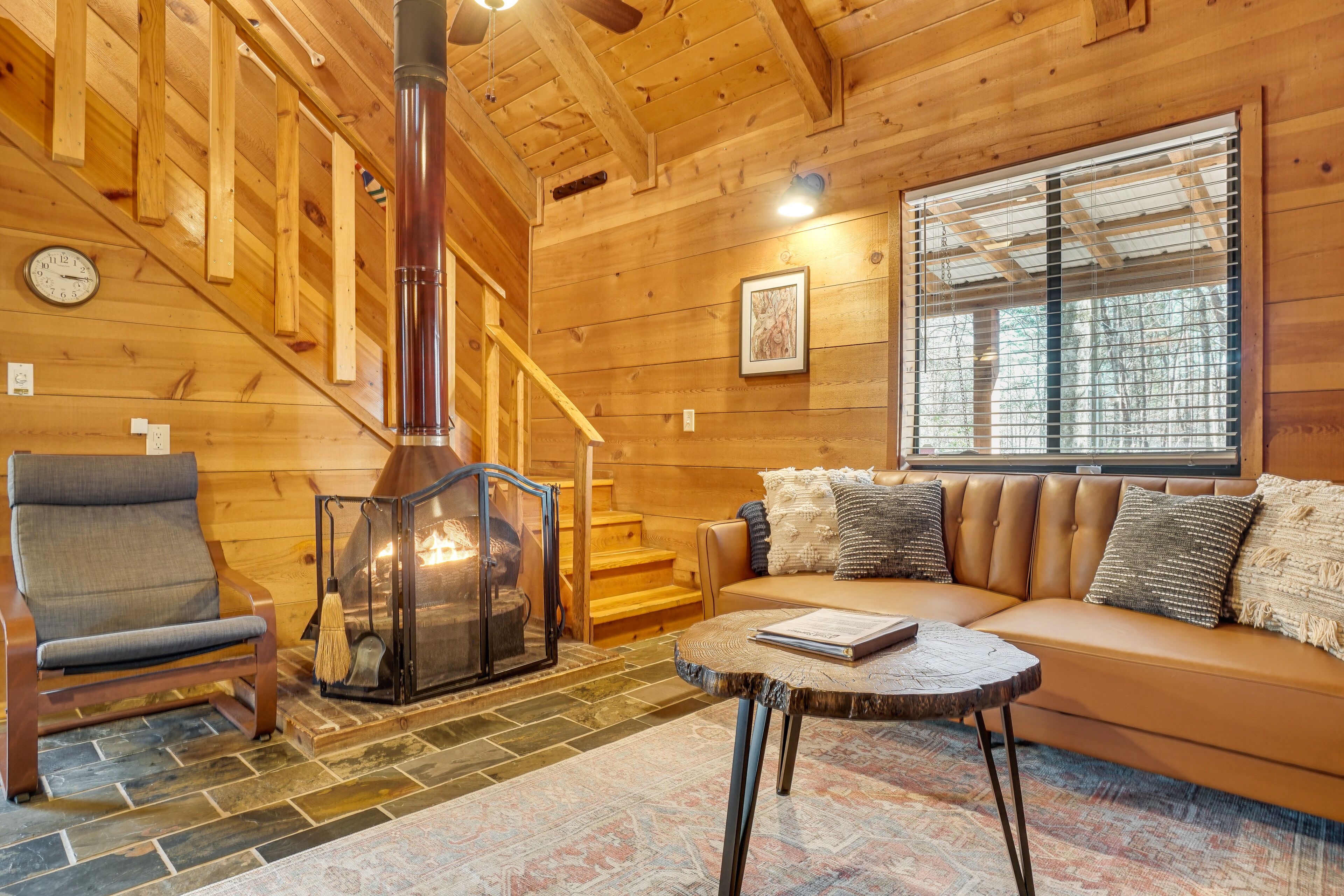 A cozy cabin interior with a fireplace, a sofa, a chair, and a staircase.