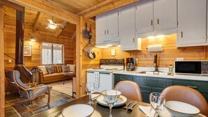 L’intérieur chaleureux d’un chalet en bois comprend un coin repas, des murs en bois, une cheminée et une petite cuisine.