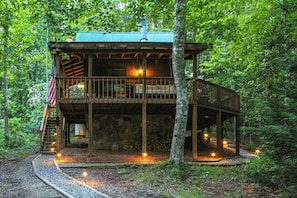 Escape to a secluded cabin surrounded by a forest, featuring a deck, staircase, and chimney.